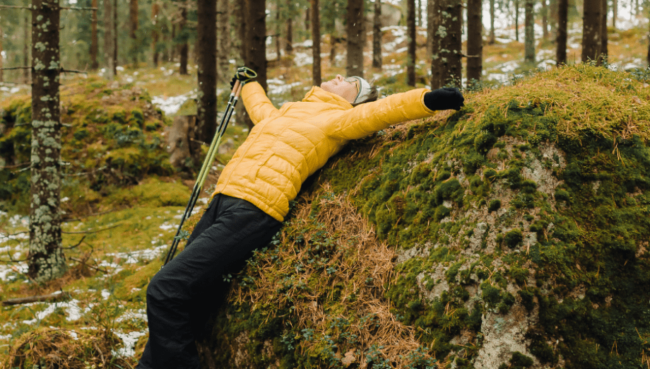Keltatakkinen nainen makaa kivellä kädet levitettynä sivuille ja hymyilee.
